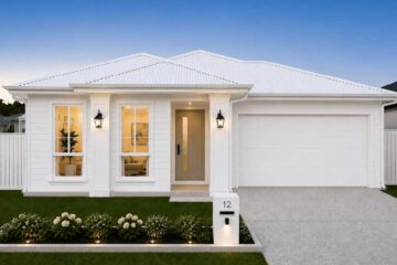 Front view of a white, single‑story house with a two‑car garage, central entry door, and lit wall lamps at dusk/evening lighted scene.